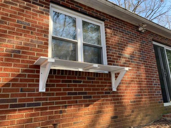 A window, mid-construction, with the floor of the catio supported by two white wooden brackets.